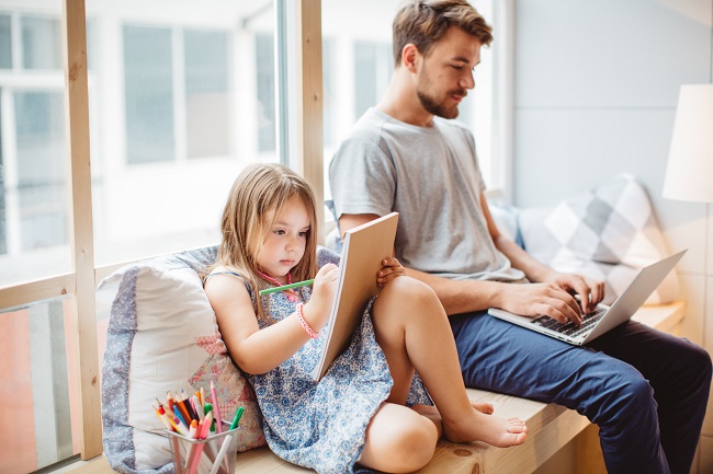 Un père travaille à côté de a fille qui dessine
