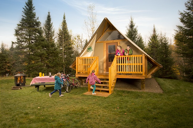 Des parents sont debout devant une tente oTENTik et des filles courent vers eux, mois d'octobre, camping de Rivière à la Pêche, Parc national de La Mauricie / Parents on deck in front of oTENTik tent and girls running towards them in October, Rivière à la Pêche campground, La Mauricie National Park