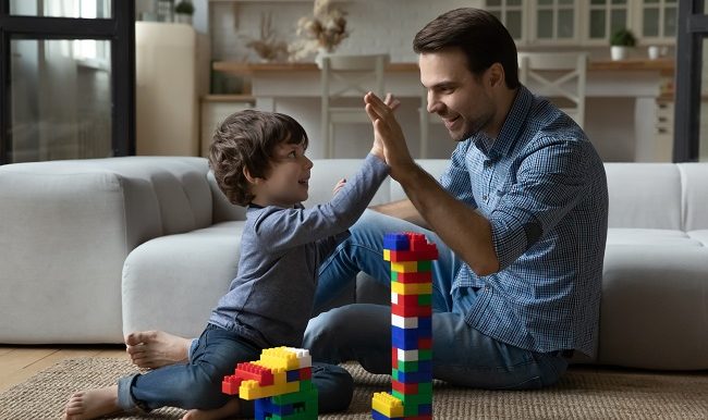 pere et son fils se font un high five après avoir réussi une tour en bloc lego h