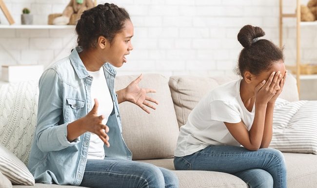 Little girl sitting on sofa crying, fighting with sister